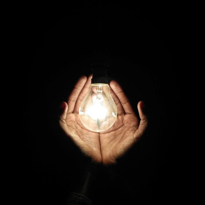 Two hands around a lit lightbulb to illusrate focusing scientific writing on impact
