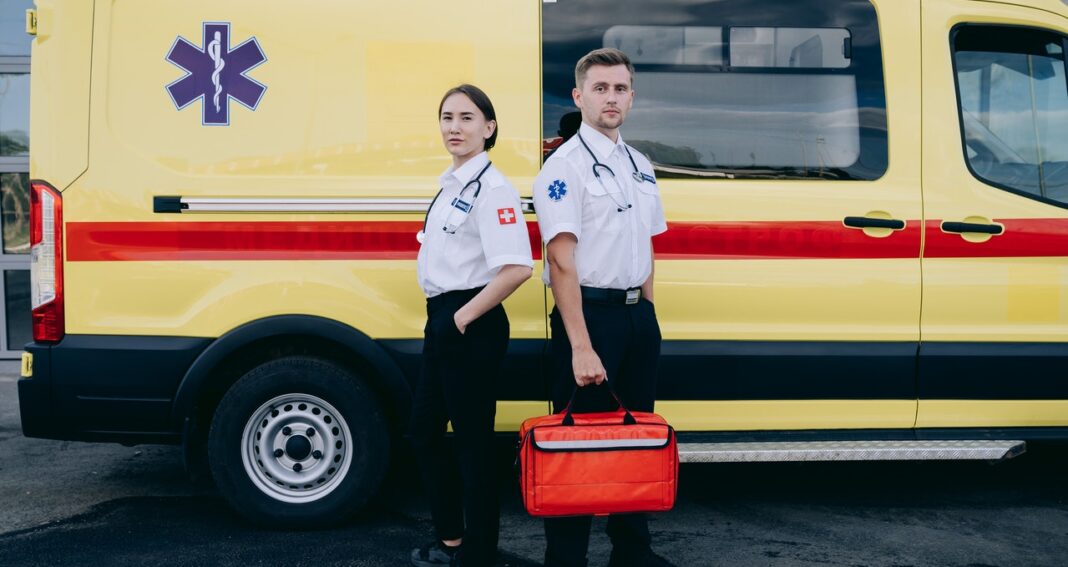two paramedics beside a yellow ambulance