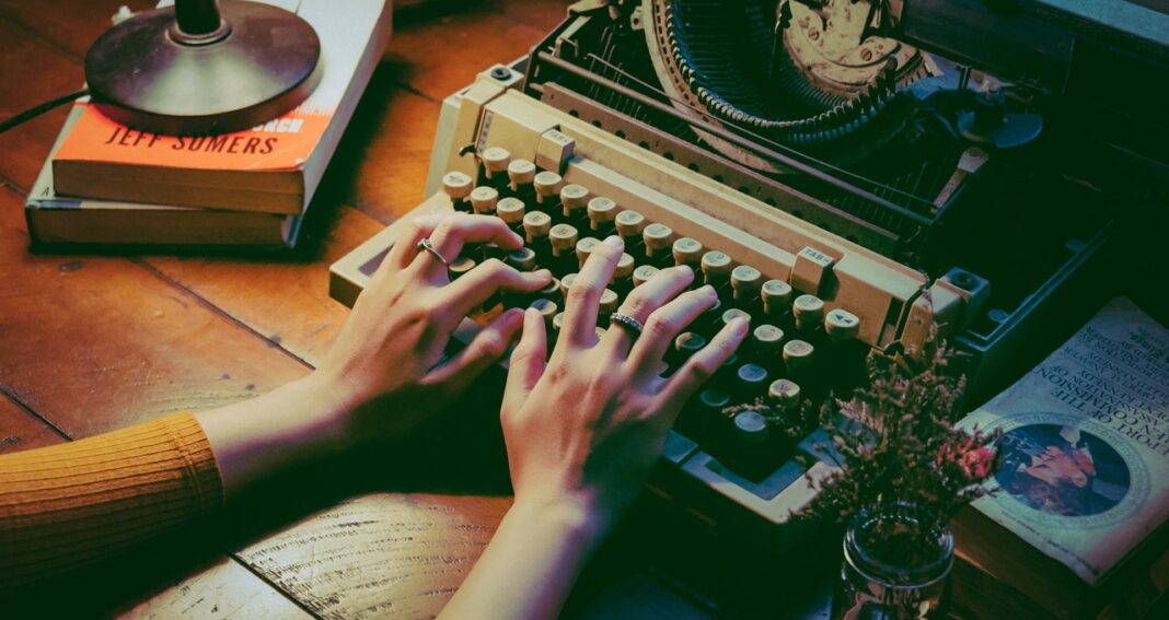 Woman's hands typing on an old manual typewriter sitting on an old table