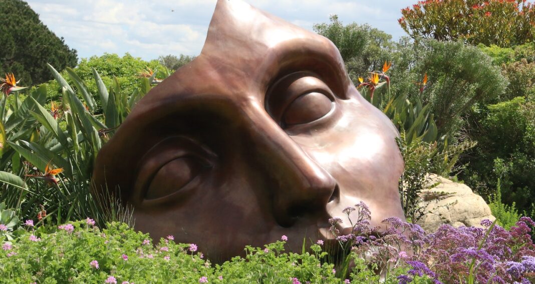 Broken brown mask with top of head missing outside in a field of flowers.