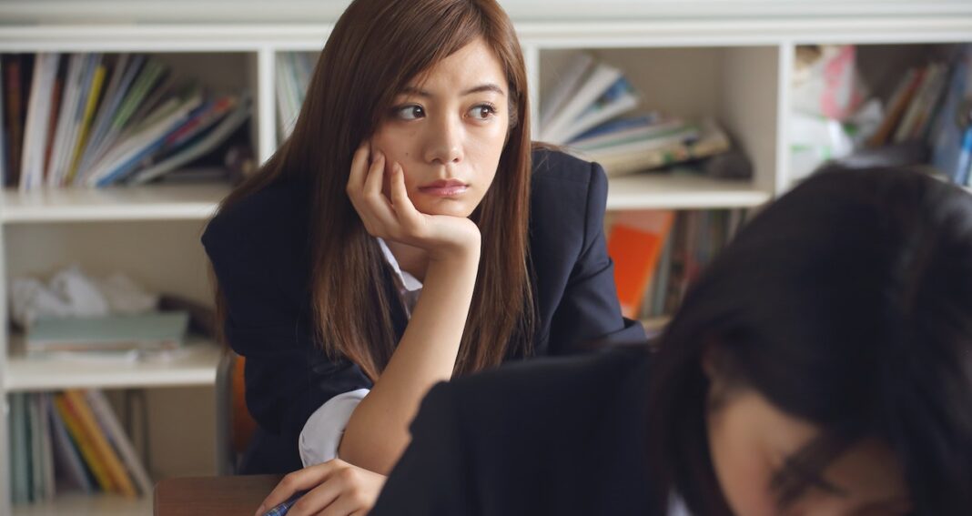 Contemplative young woman sitting in class with head in hand looking to the left.
