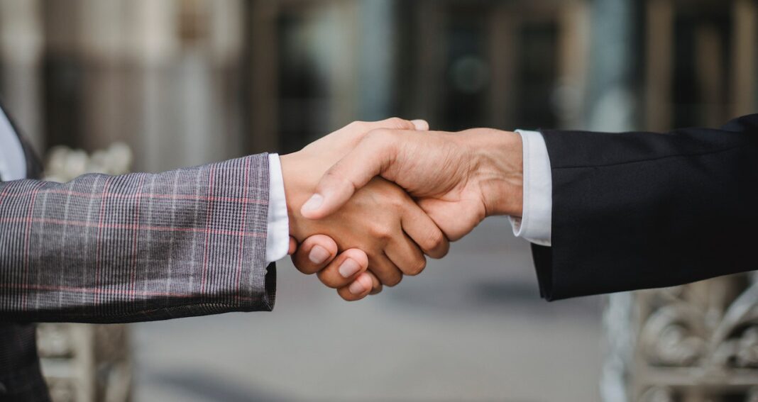 Two people shaking hands. We see only the hands with wrists covered by suit jackets.