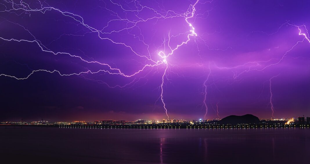 Lightning strike in a purple sky over the water.