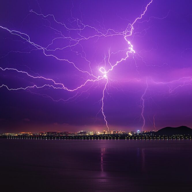 Lightning strike in a purple sky over the water.