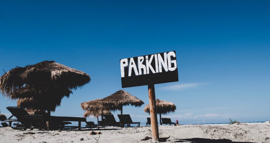 A beach with straw umbrellas and a PARKING sign in front.